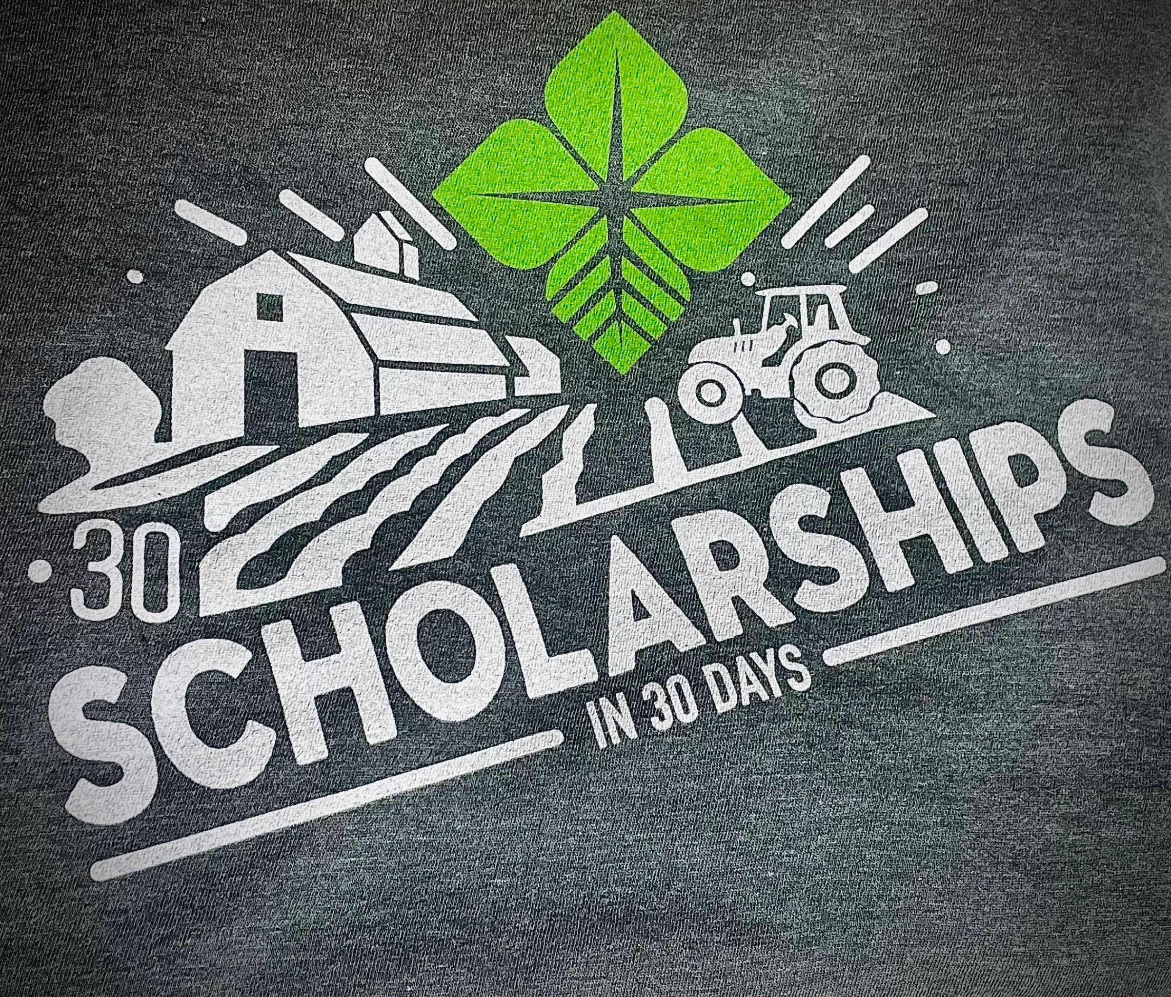 A heather charcoal tee printed with a farm scene, tractor and four-leaf mark above the words 30 Scholarships in 30 Days