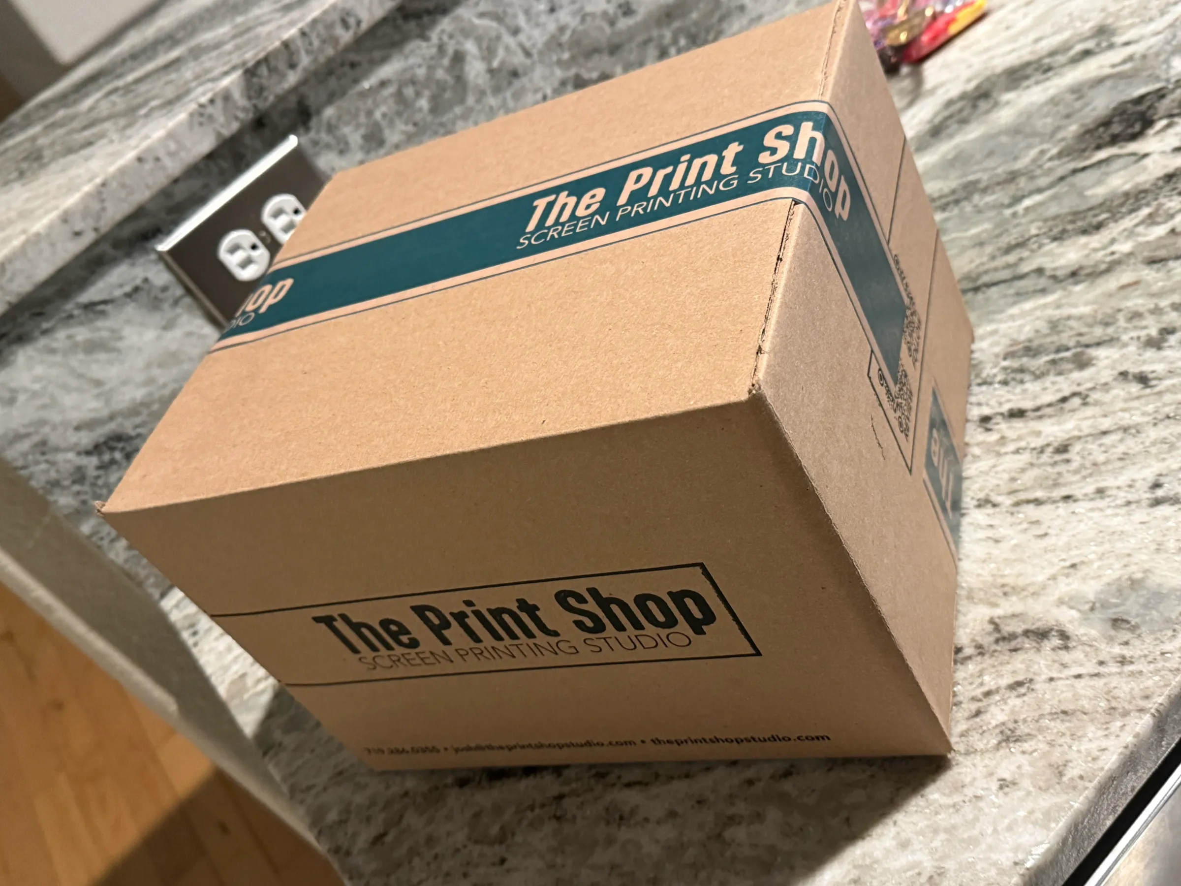 A finished order packed in a branded kraft box printed with The Print Shop — Screen Printing Studio