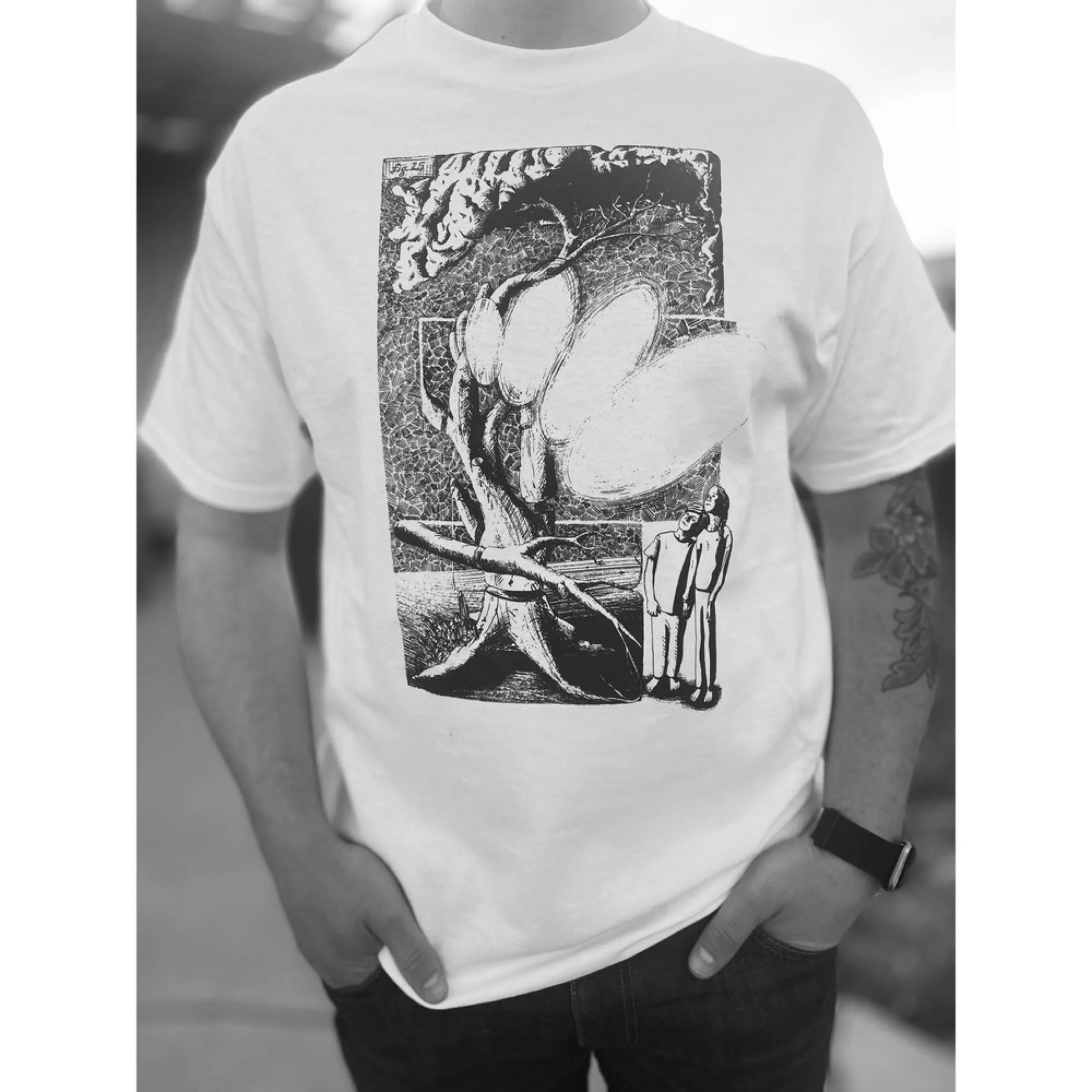 A white tee printed with Synthesis of the Aberration — a detailed pen-and-ink illustration of two figures beneath a fallen tree