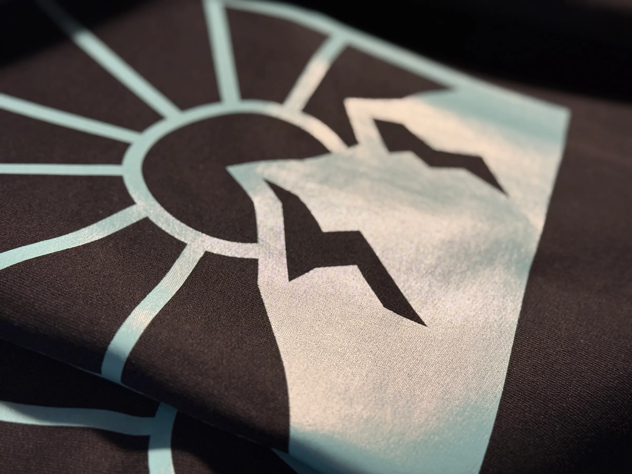Extreme close-up of pale mint ink laid onto black fabric, showing the weave under the print and the crisp edge of the mark